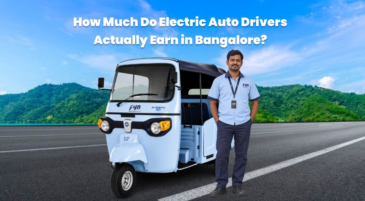 Electric auto-rickshaw with a Fyn-uniformed driver standing beside it on a road, with green hills and blue skies in the background. The image includes the text “How Much Do Electric Auto Drivers Actually Earn in Bangalore? (Real Earnings)